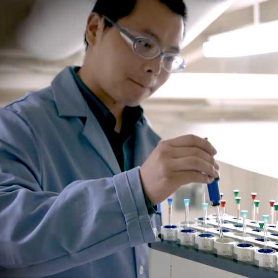 		Person in lab coat and safety glasses, placing a tube in a rack
	