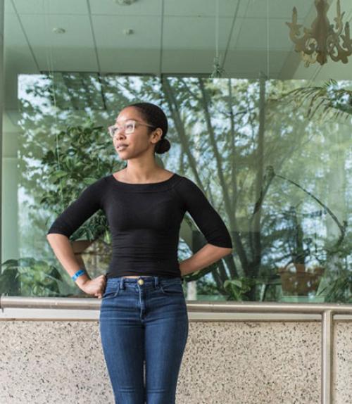 		 Dejah Powell ’18 outside Mann Library, with foliage visible in the window behind her
	