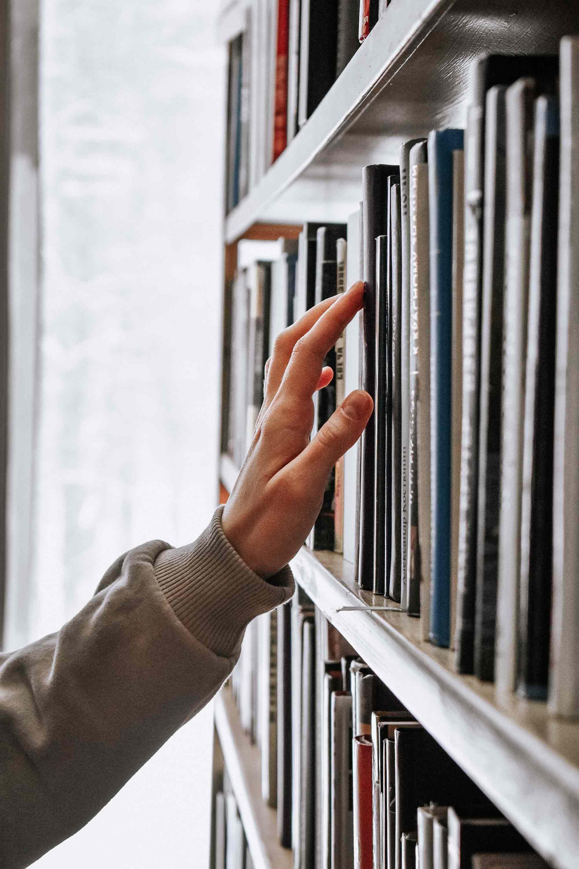		A hand reaching for a book on a bookshelf
	