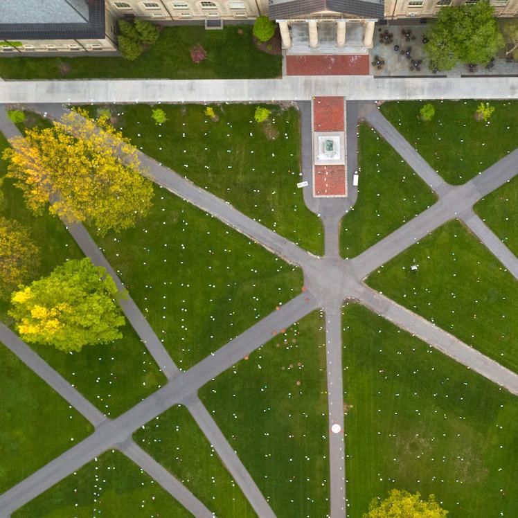 		Aerial view of Cornell's Arts Quad, showing green lawn and grey paved paths
	