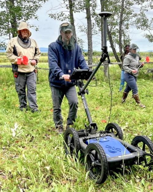 		three people use a wheeled machine on a grassy plot of land
	