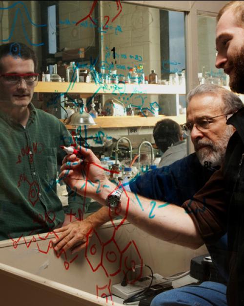 		 Hector D. Abruna, Sciences Professor of Chemistry and Chemical Biology (CHEM), in the lab with post-doctoral students writing chemistry on a white board
	