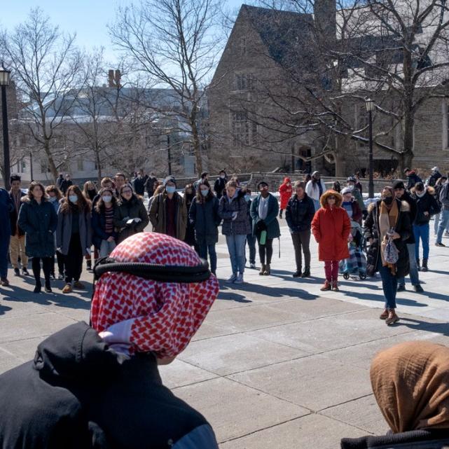 People stand in a half circle in a sunny outdoor plaza
