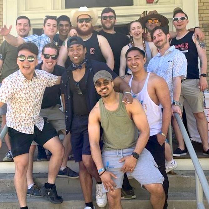 Fourteen people stand on the steps of a house, ready to party