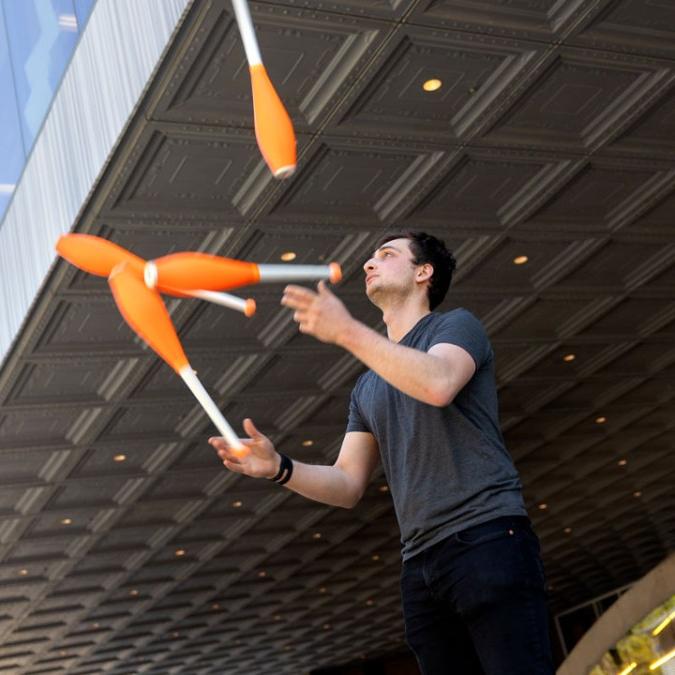 		Person juggling four orange clubs under a dark overhang
	