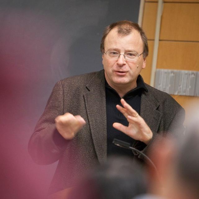 		Nicolas van de Walle speaking, hands moving, wearing glasses and a jacket
	