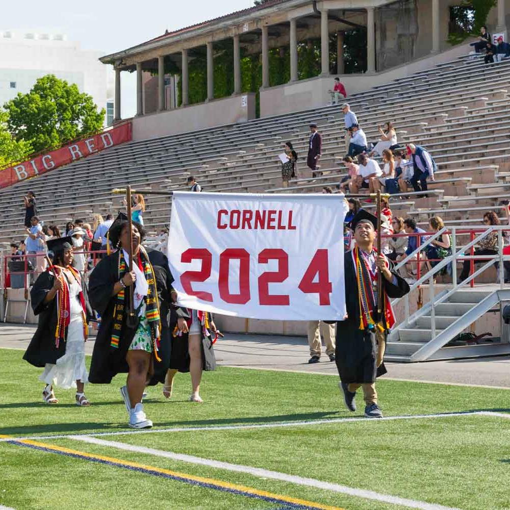 students carrying banner at graduation reading Cornell 2024