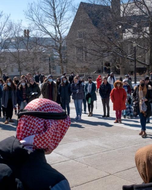 People stand in a half circle in a sunny outdoor plaza