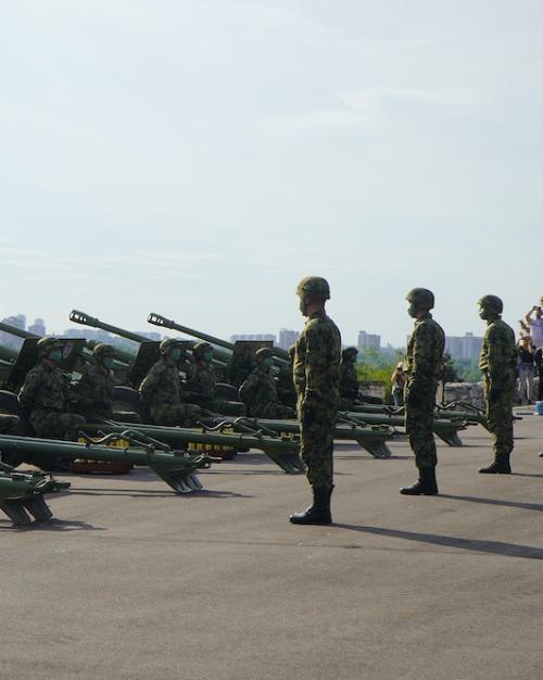 Solders stand at attention behind a row of heavy guns