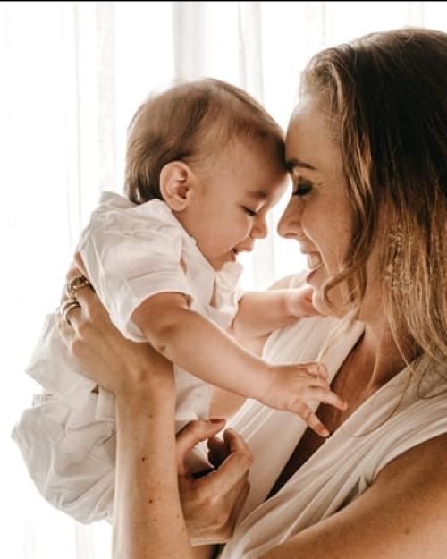Mother holding baby, leaning her forehead against the baby's forehead. Both are smiling.