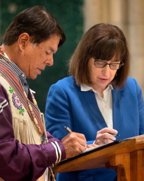 Two people sign a document on a podium