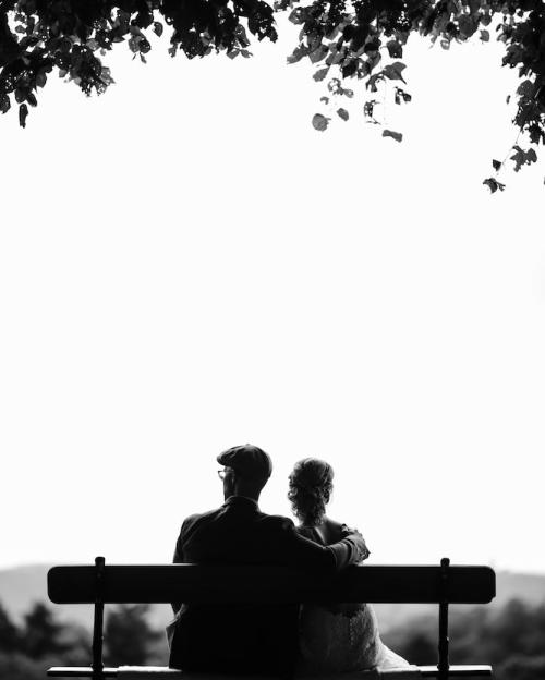 Black and white image of two people sitting on a bench, seen from behind