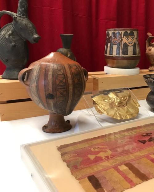 		A display case showing a ceramic head-shaped object standing on a base; a woven cloth showing animal shapes; and a gold mask
	