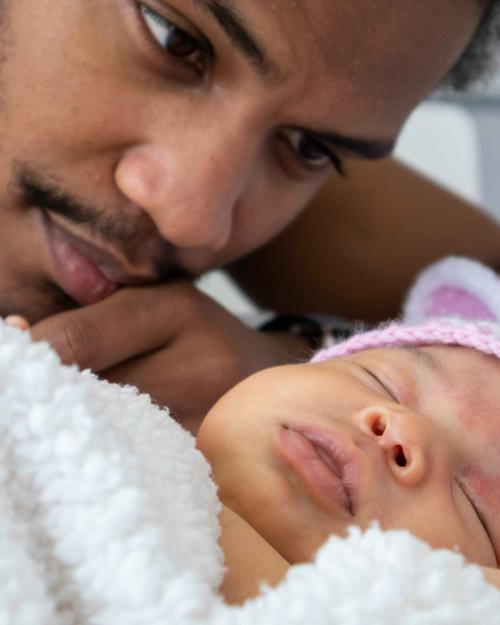 Man with mustache leaning close to sleeping baby wearing pink knitted ears