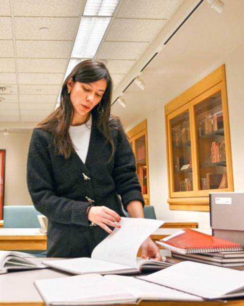 Person paging through a notebook set on a table piled with archival materials