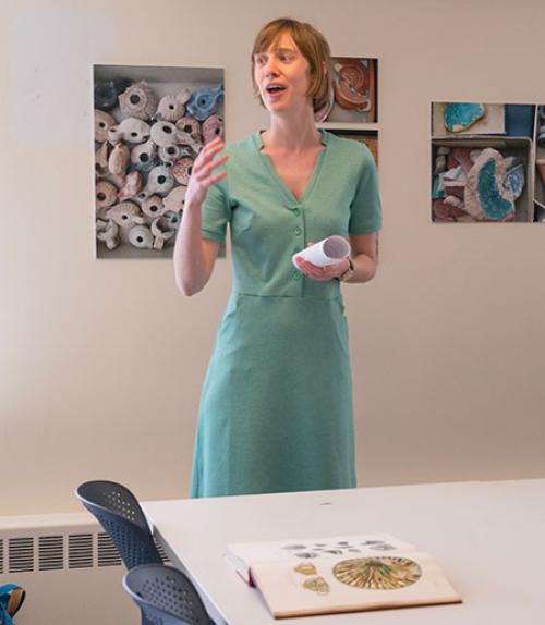  Professor Astrid Van Oyen standing in front of archaeological images on wall, welcoming everyone to lab opening