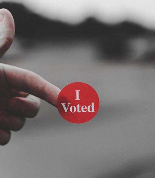  Hand holding a red sticker that says I Voted