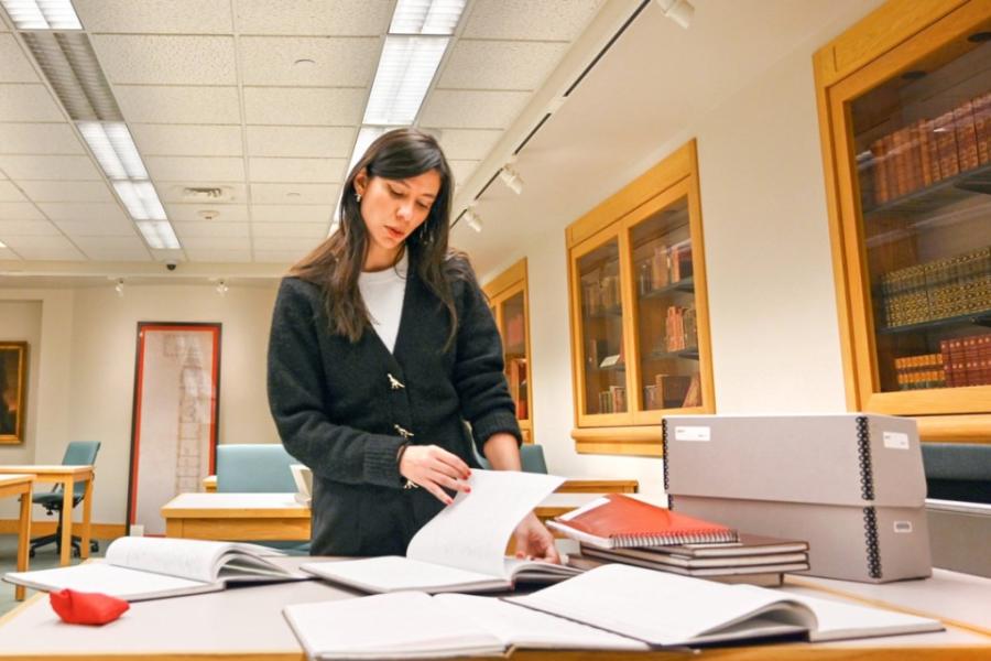 Person paging through a notebook set on a table piled with archival materials